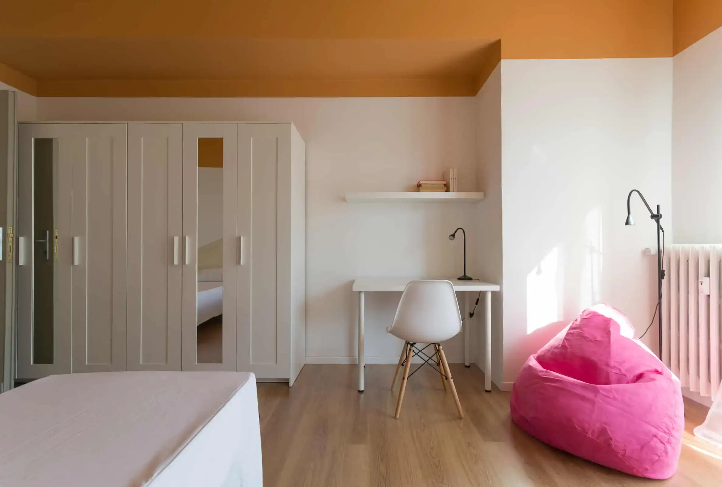 camera con scrivania e pouf rosa vicino a un armadio